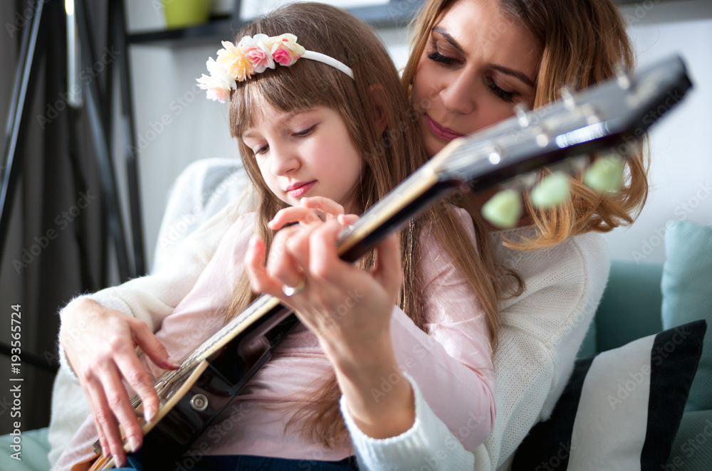 Mom with her daughter playing guitar together at home, happy family