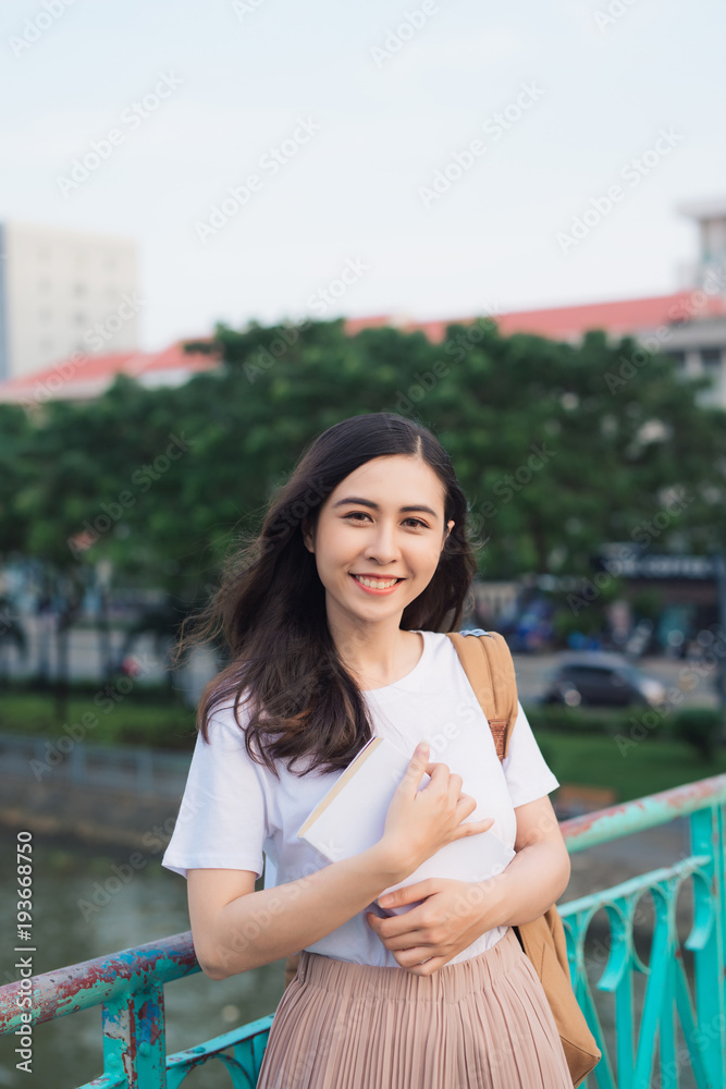 年轻漂亮的女孩在城市景观的桥上看书