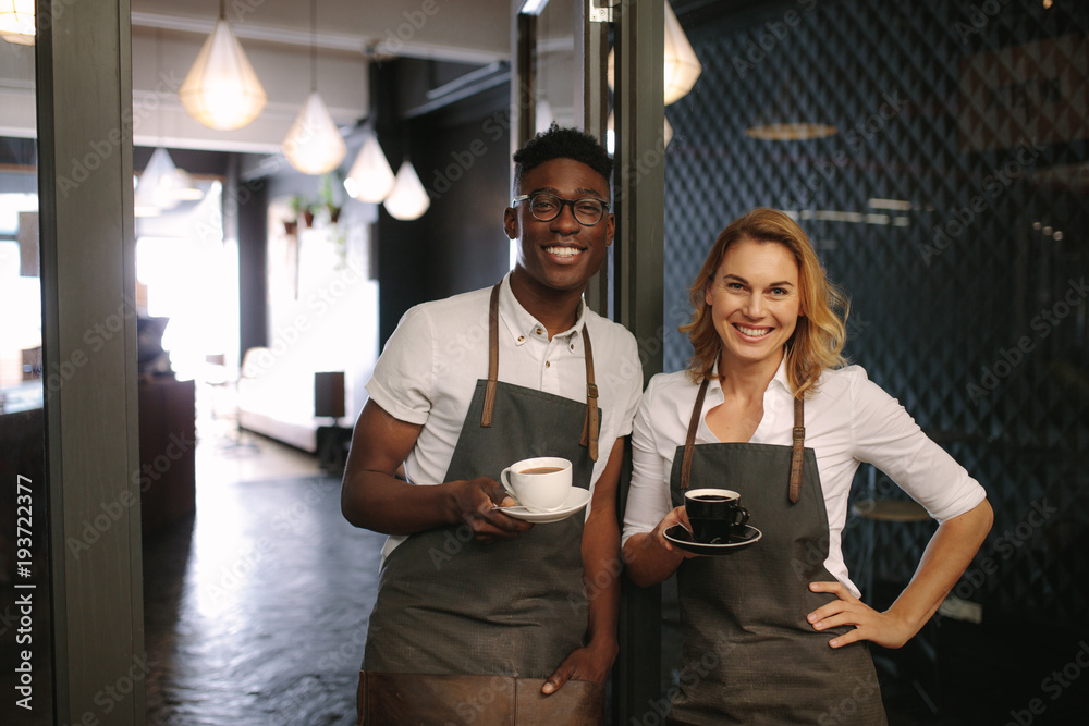 Café owners at their coffee shop holding coffee cups