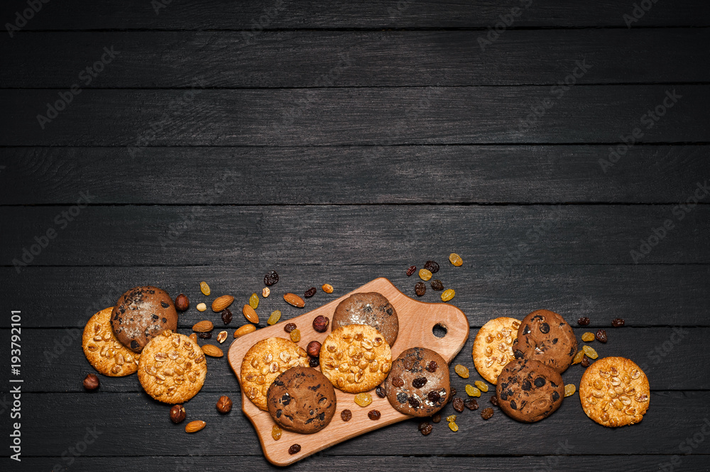 Freshly baked cookies on a wooden table. On the table is a plank, around various nuts, almonds and r