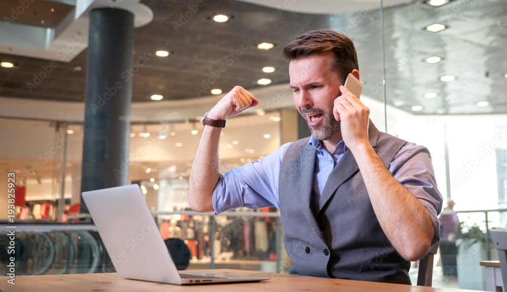 Successful businessman talking phone and using laptop showing success sign