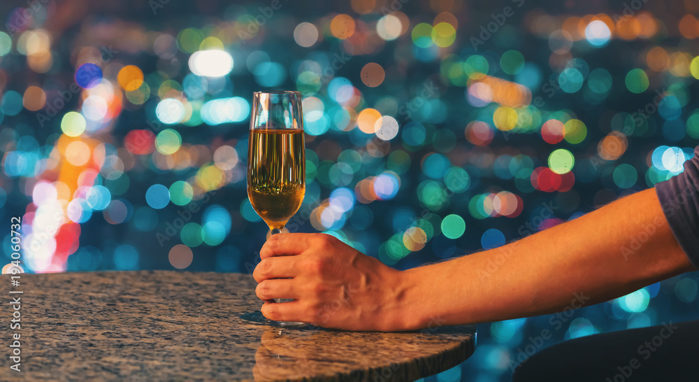 Man with a glass of white wine on a table high above the city at night