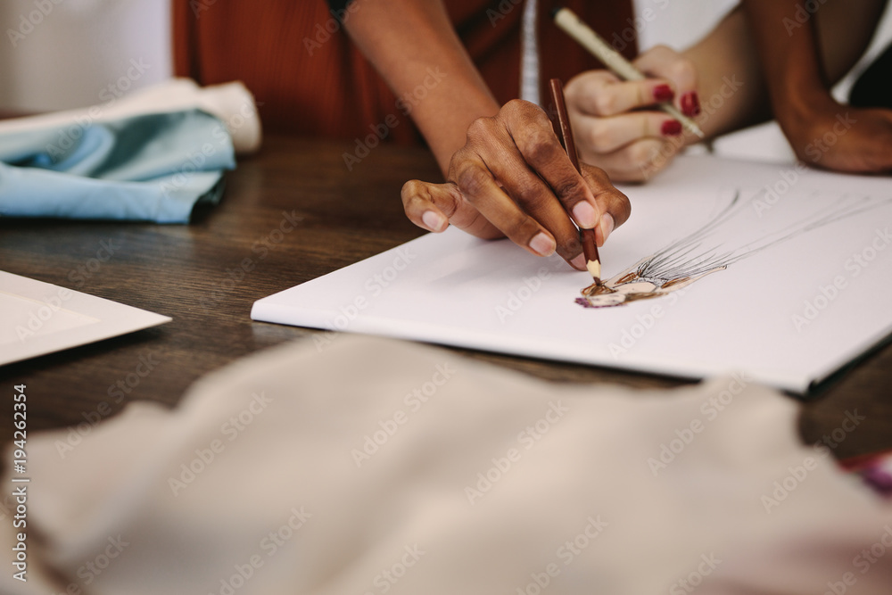 Woman fashion designers making designs on drawing paper