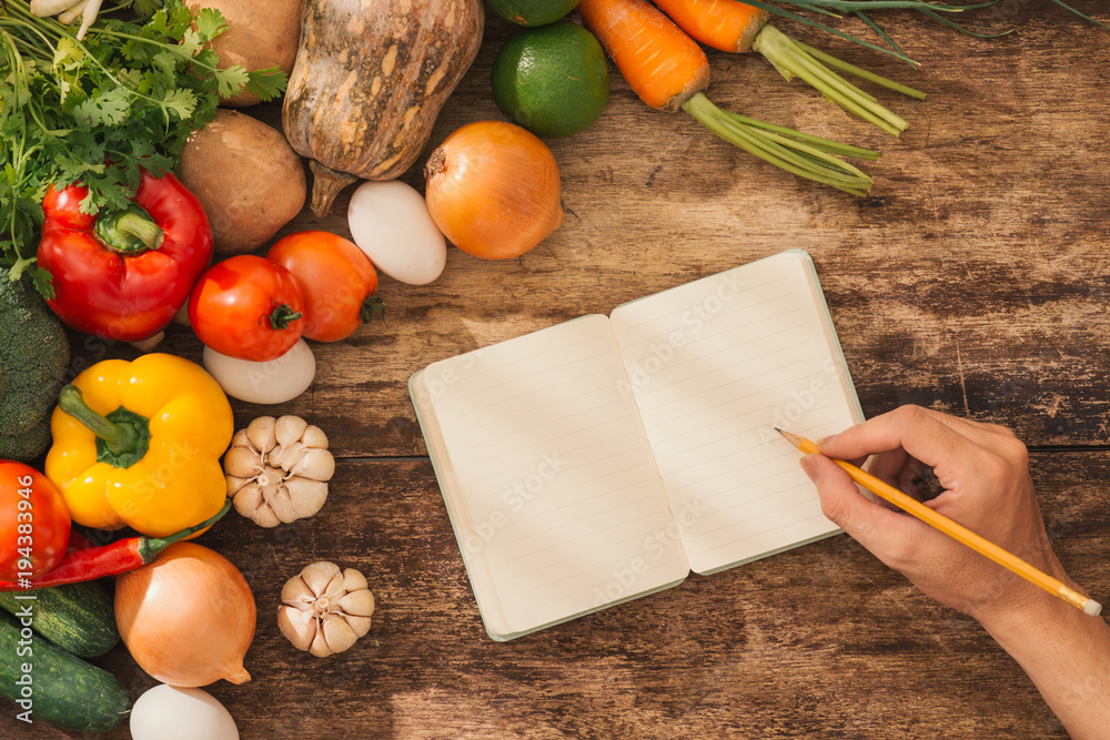 Cookbook. Fresh vegetables around open notebook on rustic background.