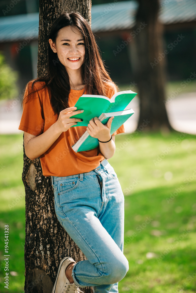 一个年轻或十几岁的亚洲女学生在大学里微笑着看书，看着平板电脑