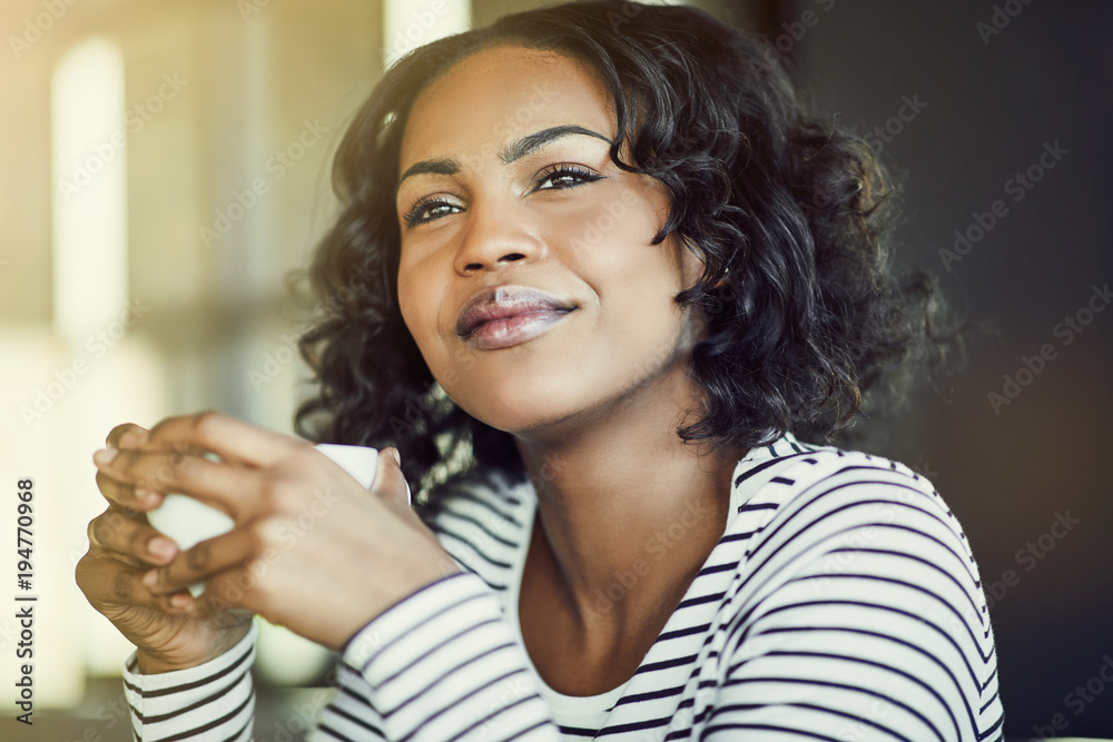 Smiling young African woman deep in thought while drinking coffe