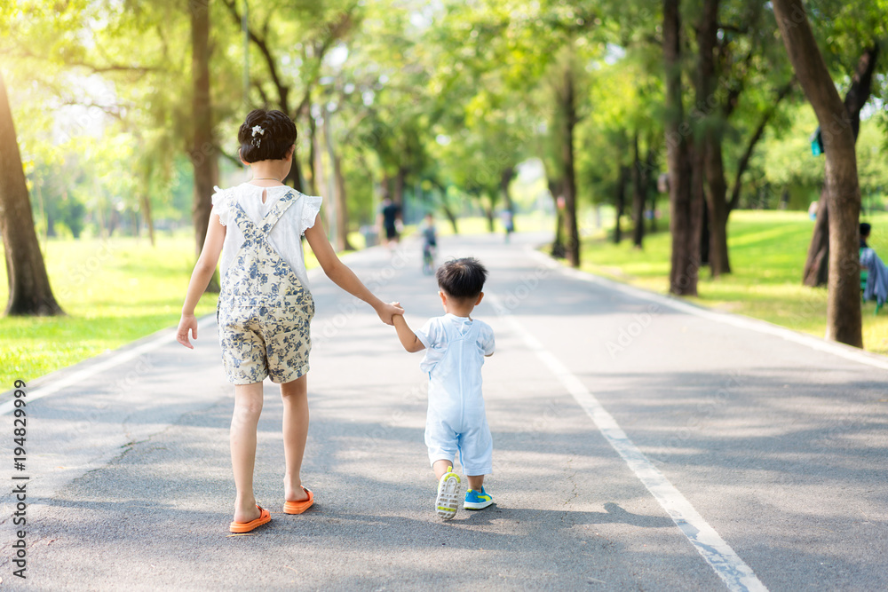 亚洲姐妹牵着走在公园里阳光明媚的路上的小孩。