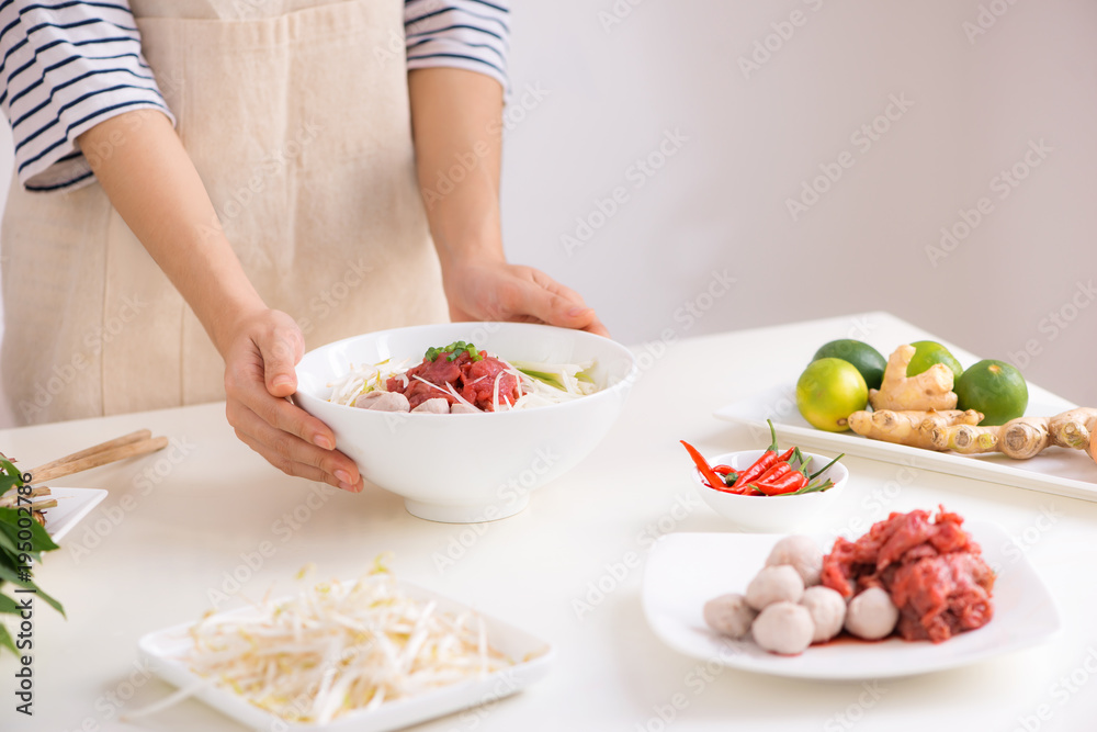 Female chef prepare traditional Vietnamese soup Pho bo with herbs, meat, rice noodles