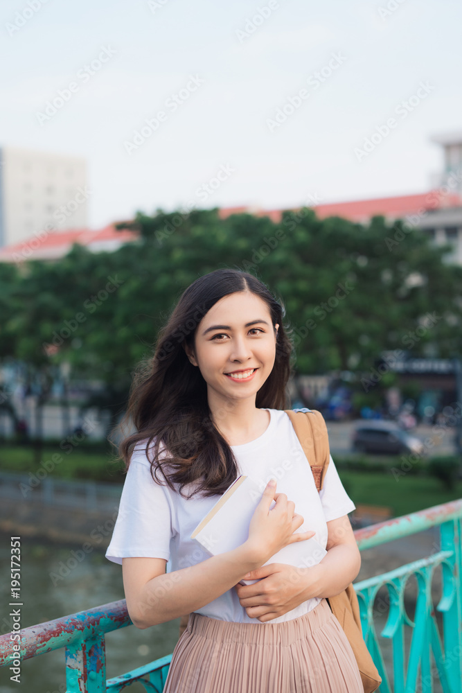 年轻漂亮的女孩在城市景观的桥上看书