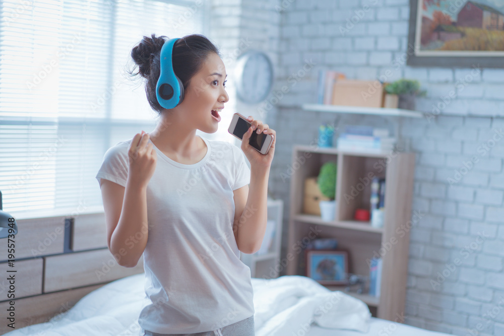 亚洲女人正在听音乐，她在房间里唱歌。很开心。