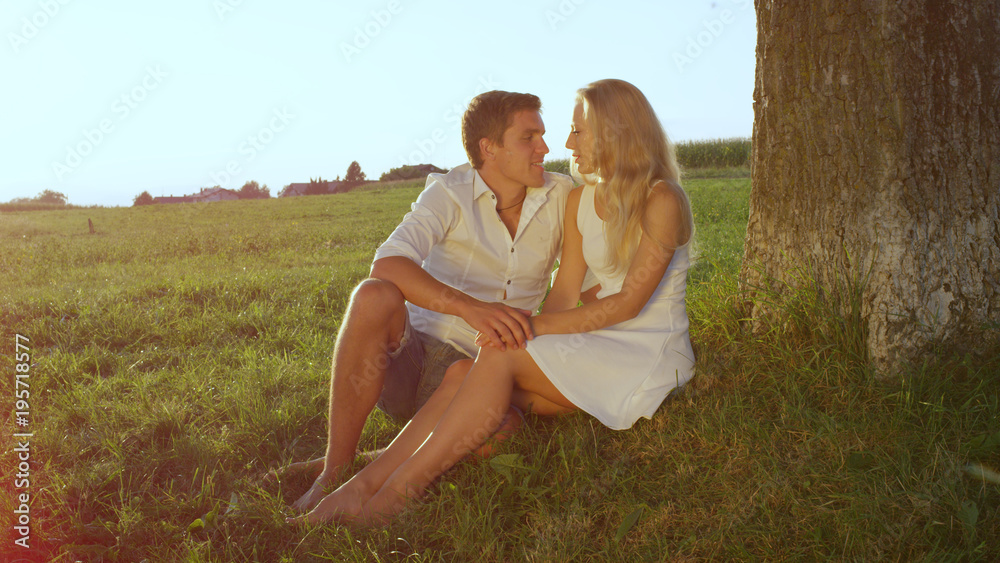 LENSE FLARE: Embraced young couple sharing an intimate moment in a sunlit meadow