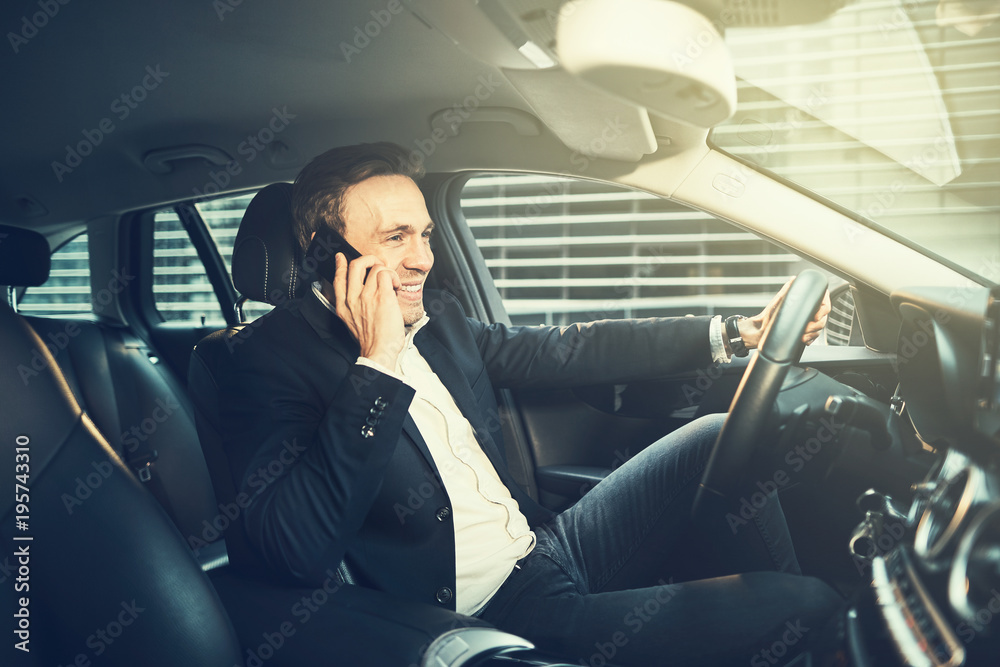 Smiling businessman talking on a phone in his car