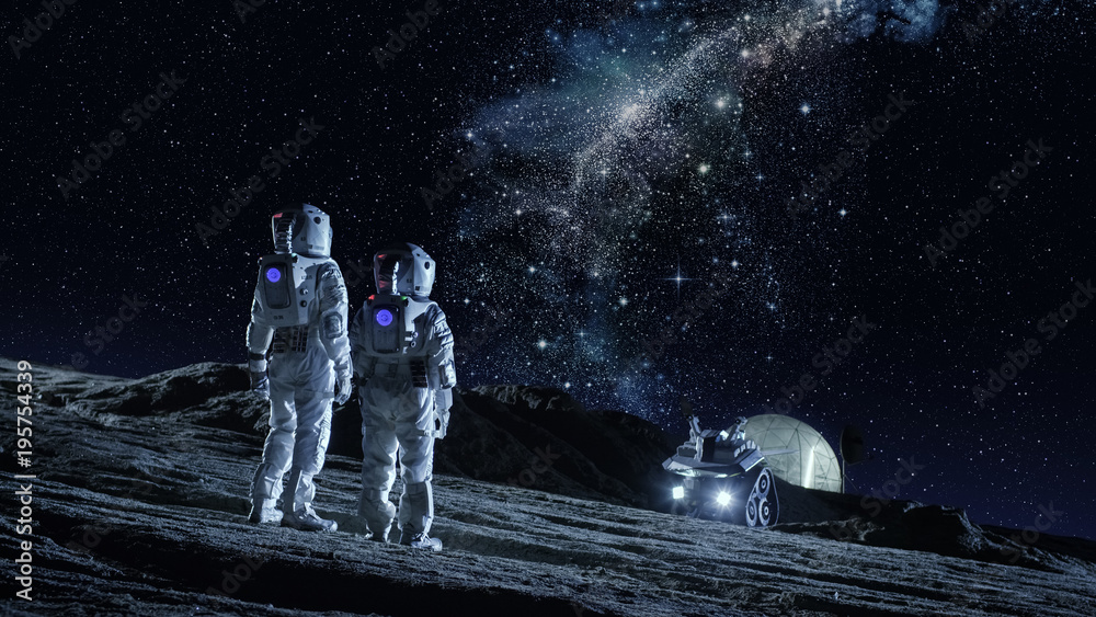 Two Astronauts in Space Suits Stand on the Planet and Looking at the The Milky Way Galaxy. In the Ba