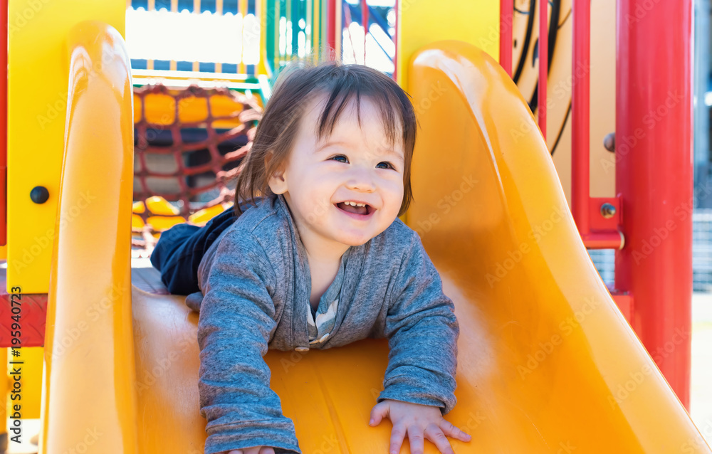 Happy toddler boy playing on a slide at a playground