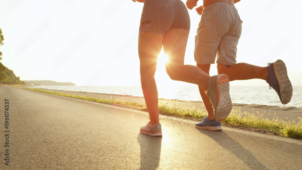 阳光灿烂年轻的面目全非的女人和男人沿着海洋进行可爱的奔跑