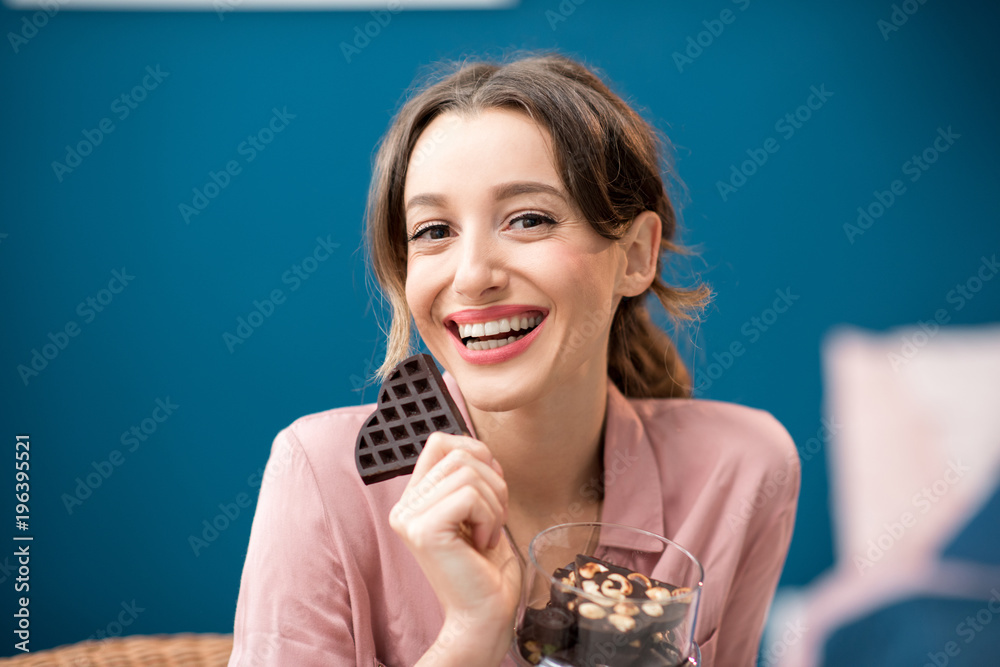 Beautiful woman enjoying a chocolate sitting on the blue wall background indoors