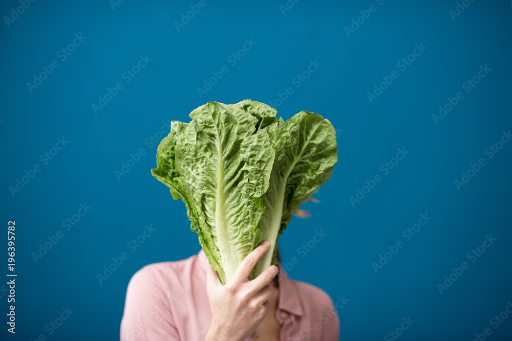 Portrait of a young woman with green lettuce on the blue wall background