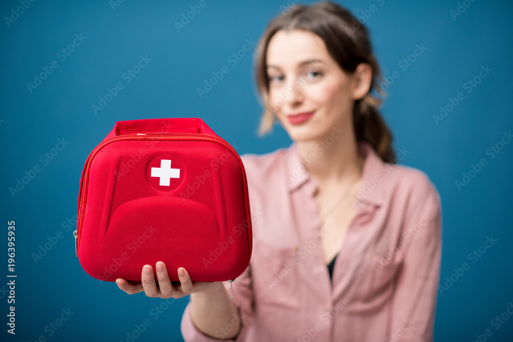 Portrait of a woman with first aid kit on the blue wall background