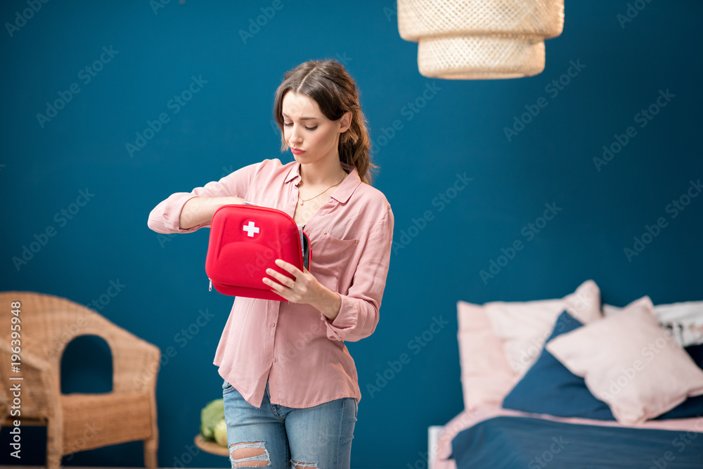 Woman getting a pills from first aid kit standing indoors in the blue living room at home