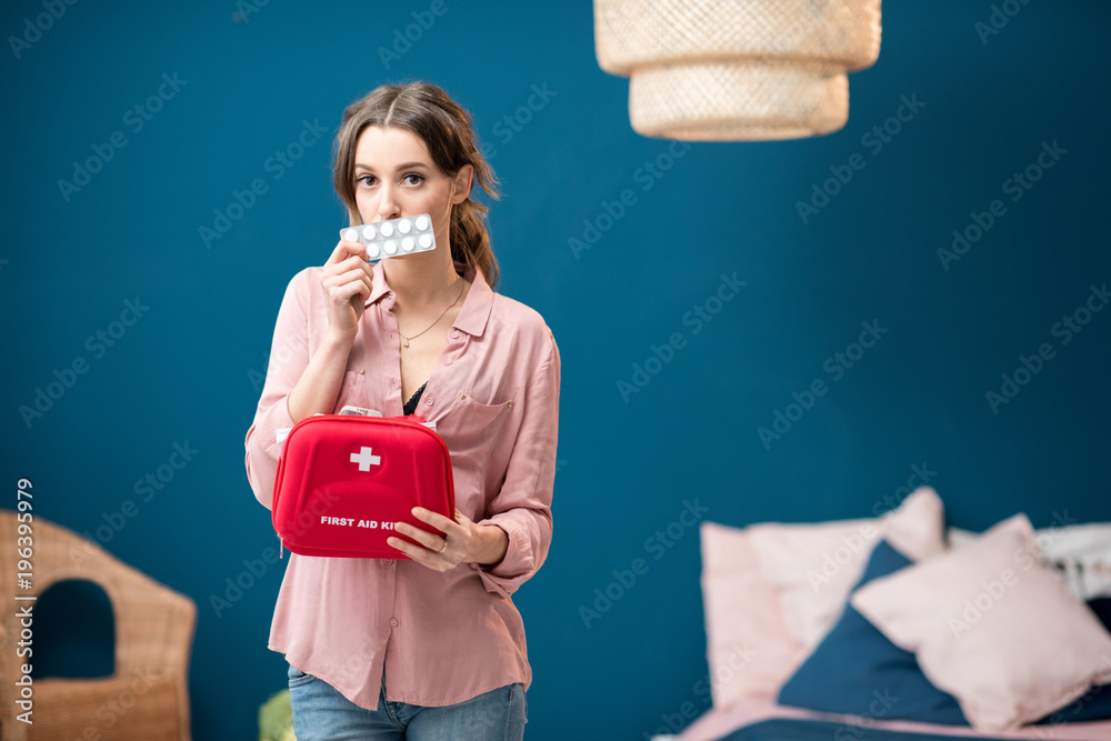 Woman getting a pills from first aid kit standing indoors in the blue living room at home