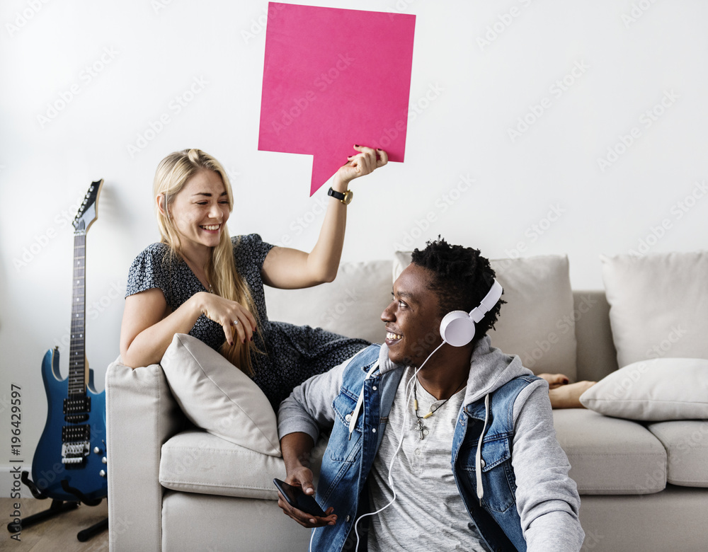 Interracial couple sharing music at home holding copyspace speech bubble