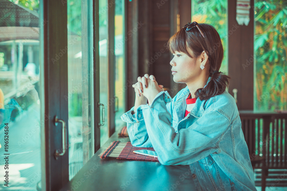 泰国清迈，一位身穿牛仔衬衫的亚洲美女坐在咖啡店外眺望