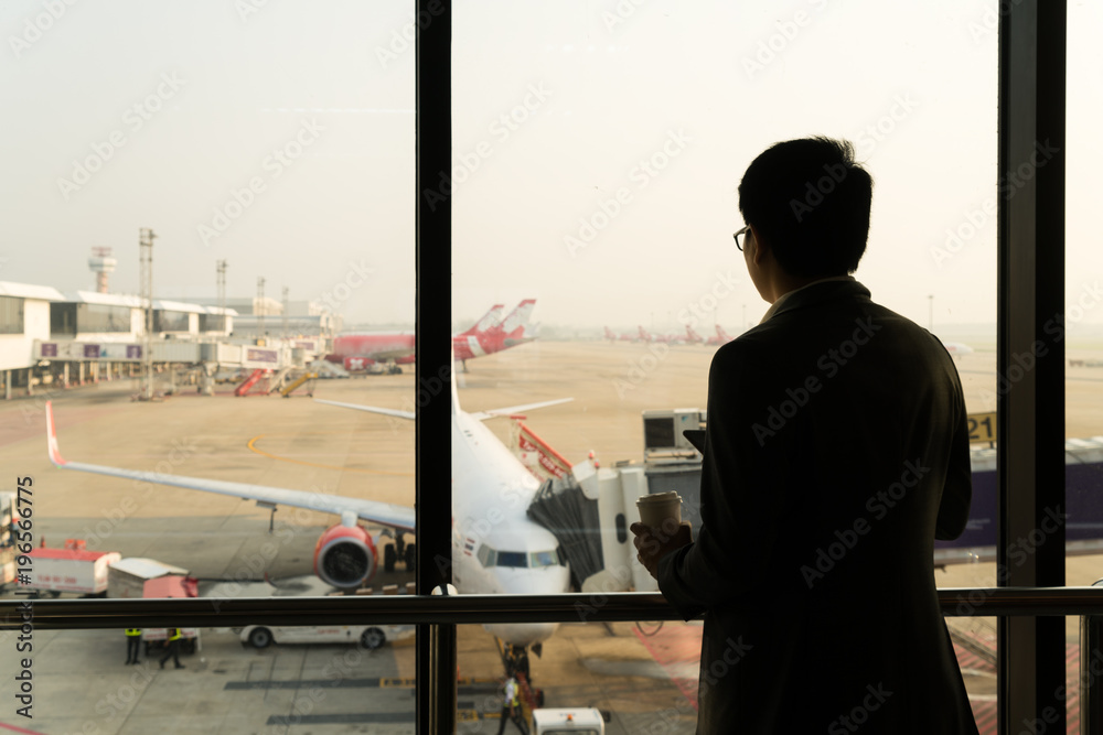 Young businessman stand at terminal in internatianal airport during sunset and chatting on the phone