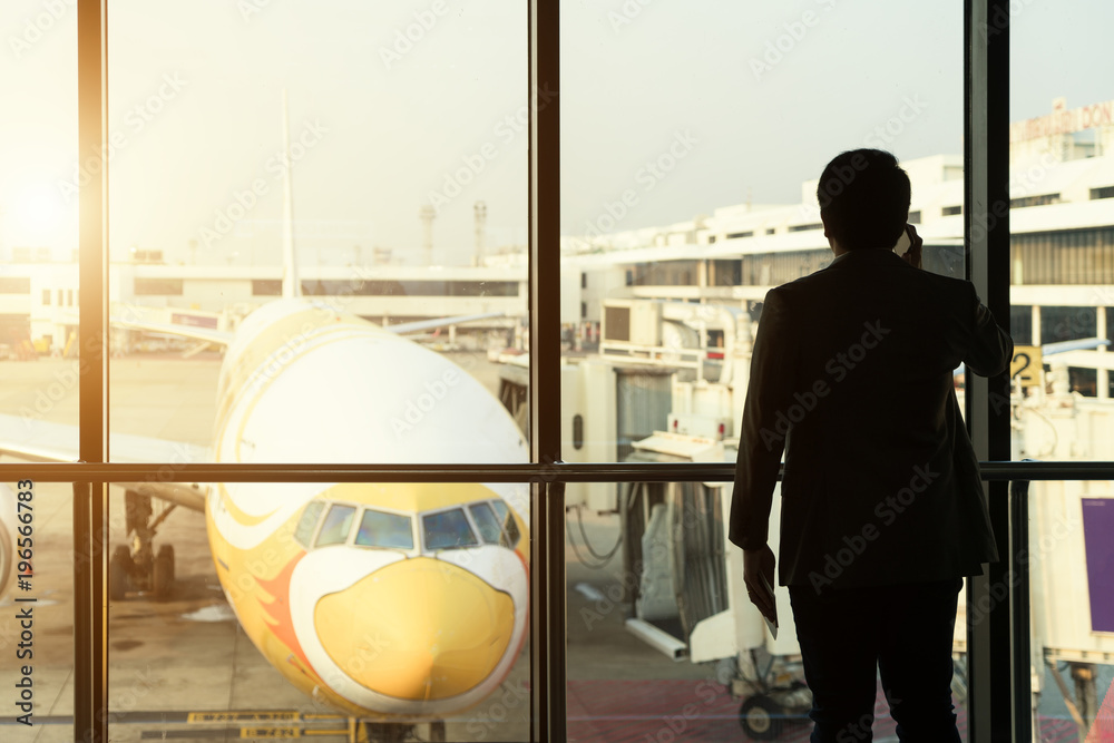 Young businessman stand at terminal in internatianal airport during sunset and talking on the phone 