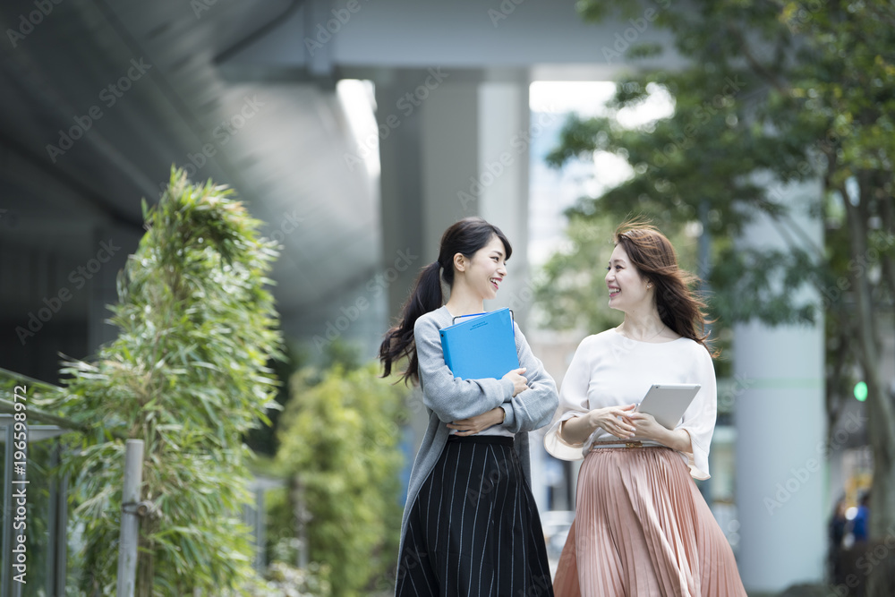 資料とタブレットを持って外を歩く女性たち