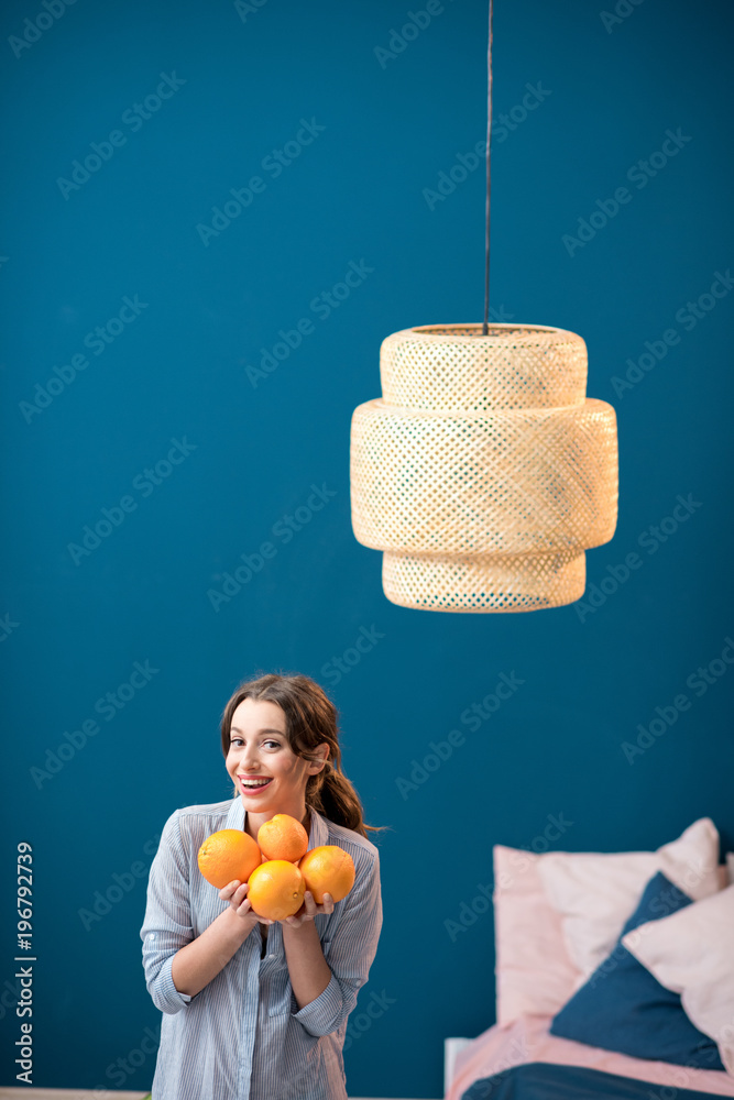 Portrait of a young and happy woman with oranges on the blue wall background at home