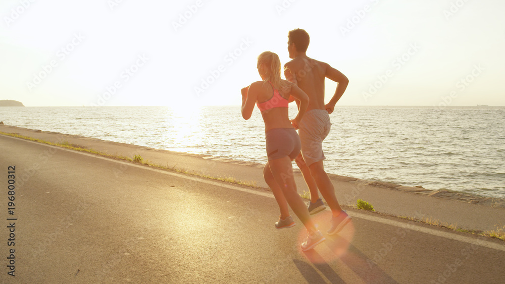 SUN FLARE: Lovely young couple jogs down ocean road on perfect summer afternoon.