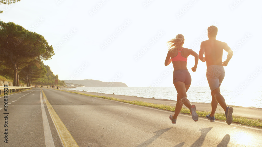 COPY SPACE: Athletic young couple jogging near the sea on perfect day in summer