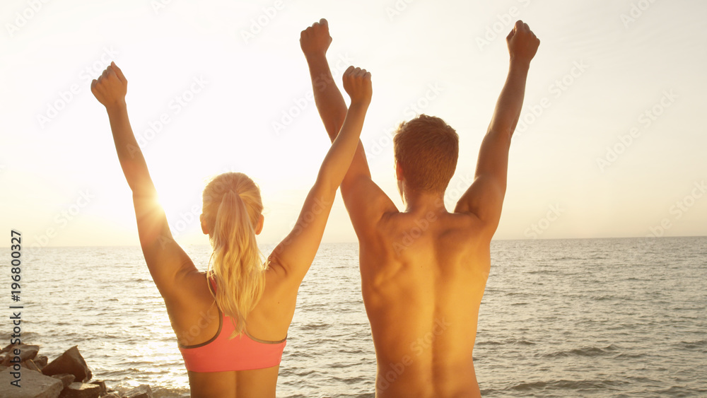 CLOSE UP, SUN FLARE: Joyous young couple outstretch their arms after fun run