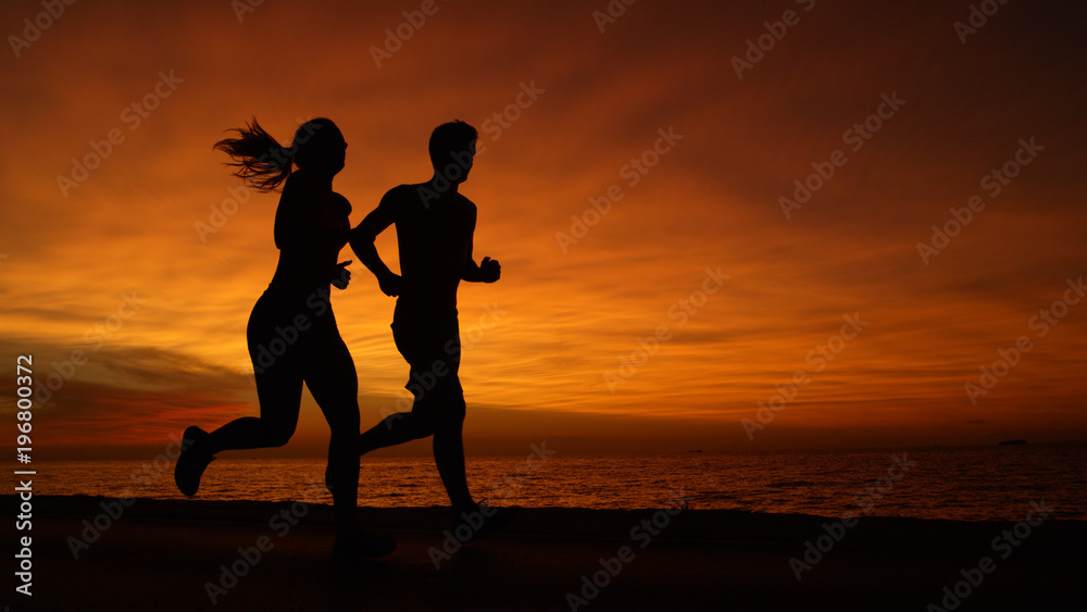 COPY SPACE: Athletic Caucasian couple jogs down scenic ocean road at sunrise.