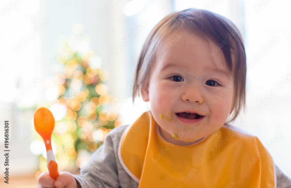 Happy little baby boy eating food in his house