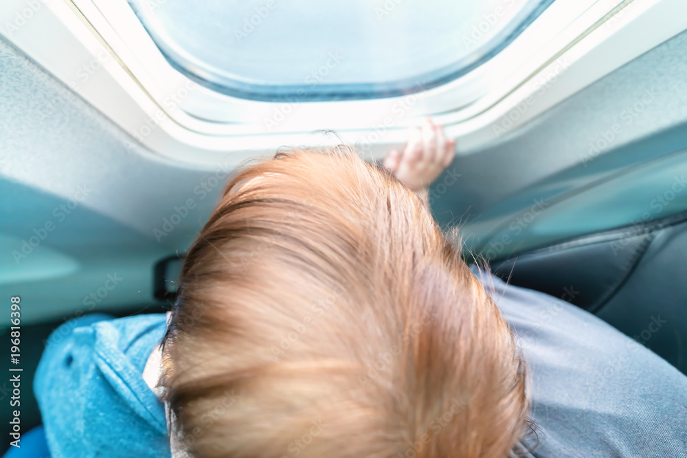 Little toddler boy looking out an airplane window while flying