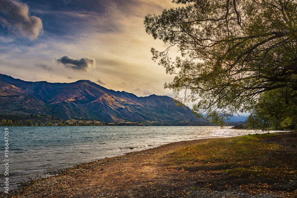 Sunset on lakeside of Wanaka, New Zealand with mountain, golden sky and lake.