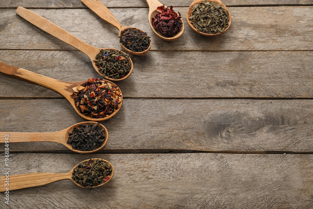 Spoons with variety of dry tea leaves on wooden background