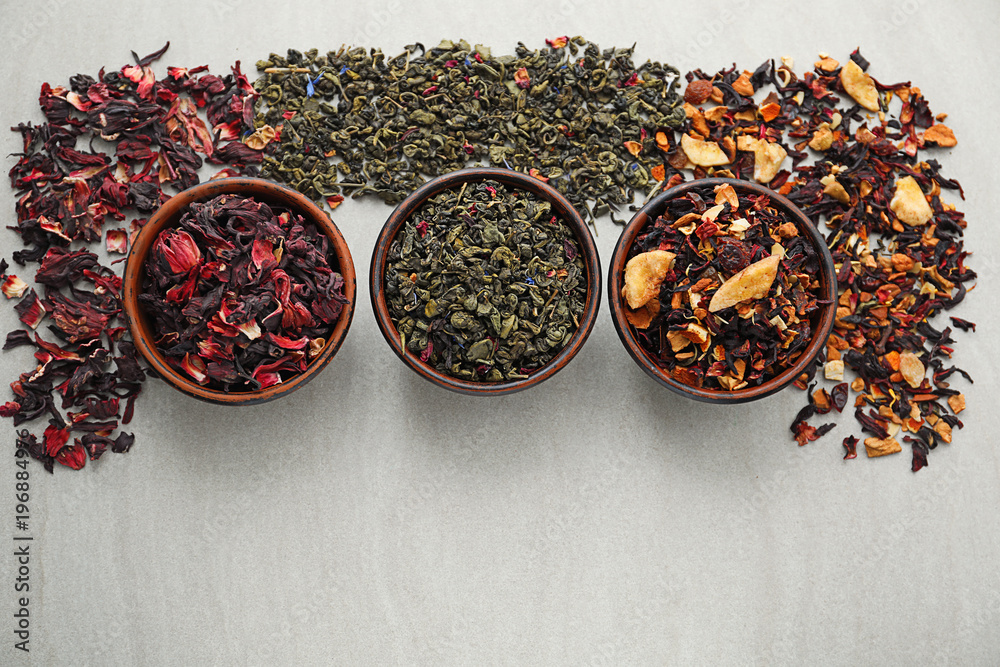 Bowls with different types of dry tea leaves on light background