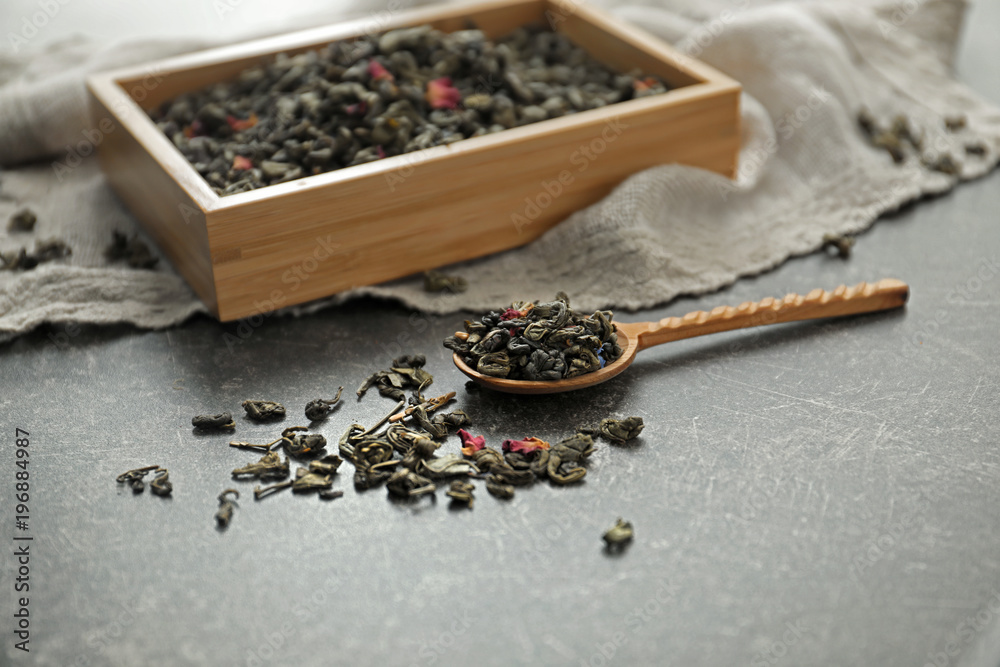 Wooden box and spoon with dry green tea leaves on table