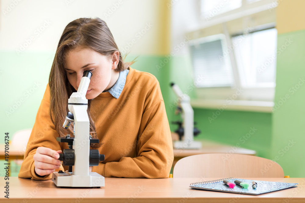 生物课上的高中女生。学生用显微镜检查样本。