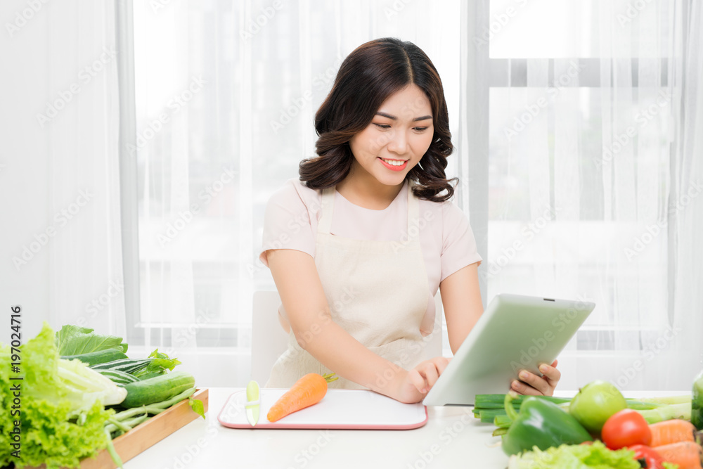 年轻女子拿着平板电脑站在厨房里，有想法，在厨房里看食谱