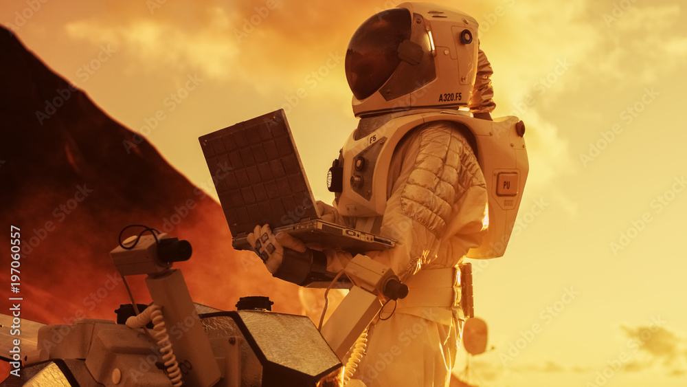 Astronaut in the Space Suit Works on Laptop, Adjusting Rover on a New Alien Red Planet, Presumably M