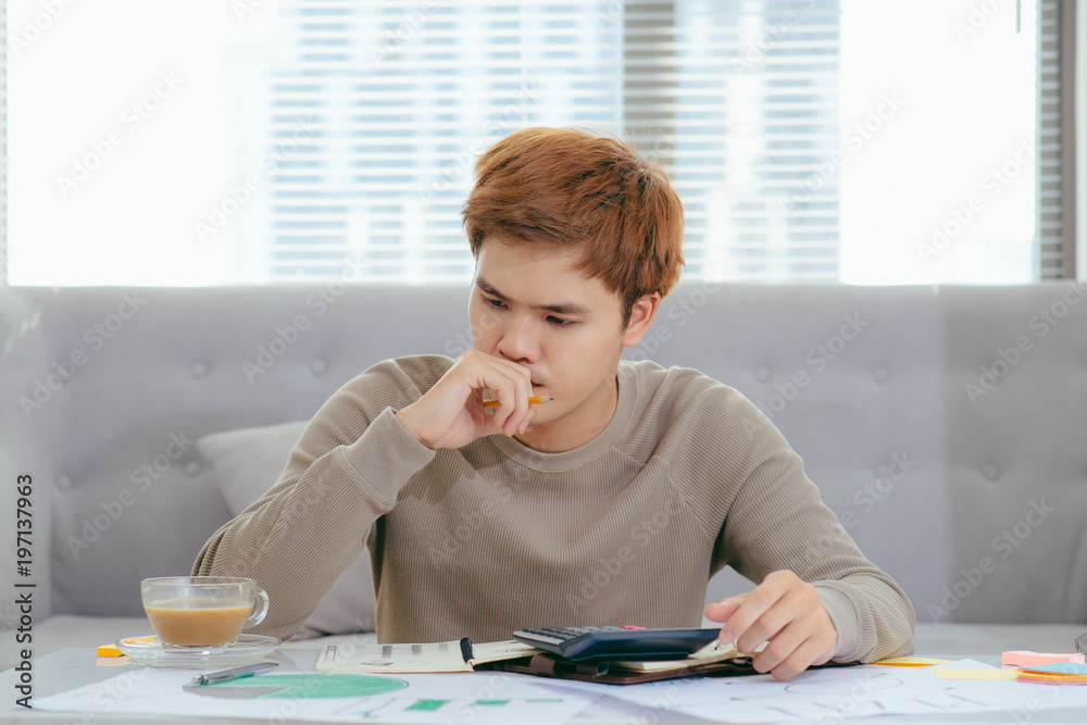 Asian man doing finances and calculate about cost at home office.