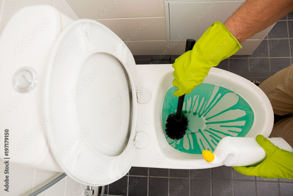 Man in rubber protective gloves cleaning and washing toilet with brush and bottle of cleaning agent 