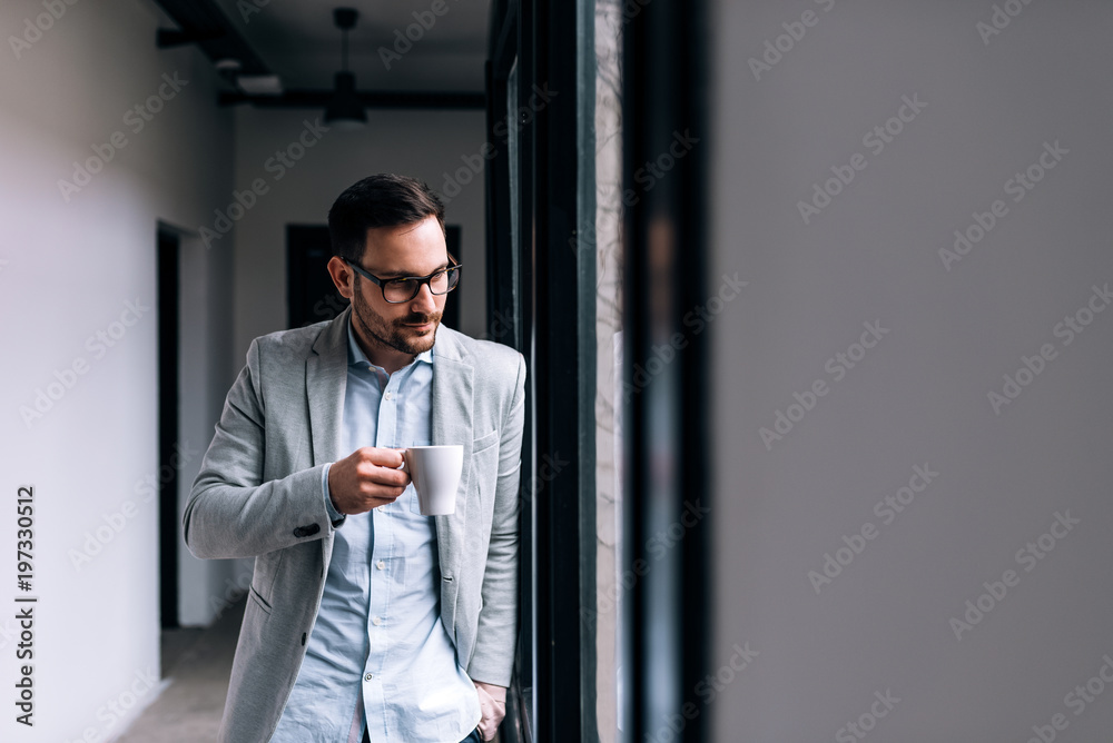 年轻的商人在工作中休息。一边喝咖啡一边透过窗户看。