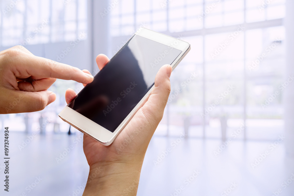 hand smartphone and finger point to screen with blur backgrpund of office hall interior