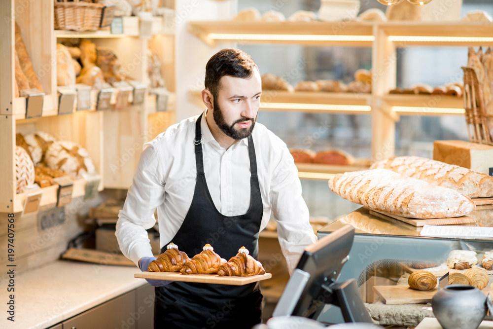 Handsome bread seller with croissants in the small and cozy store with bakery products