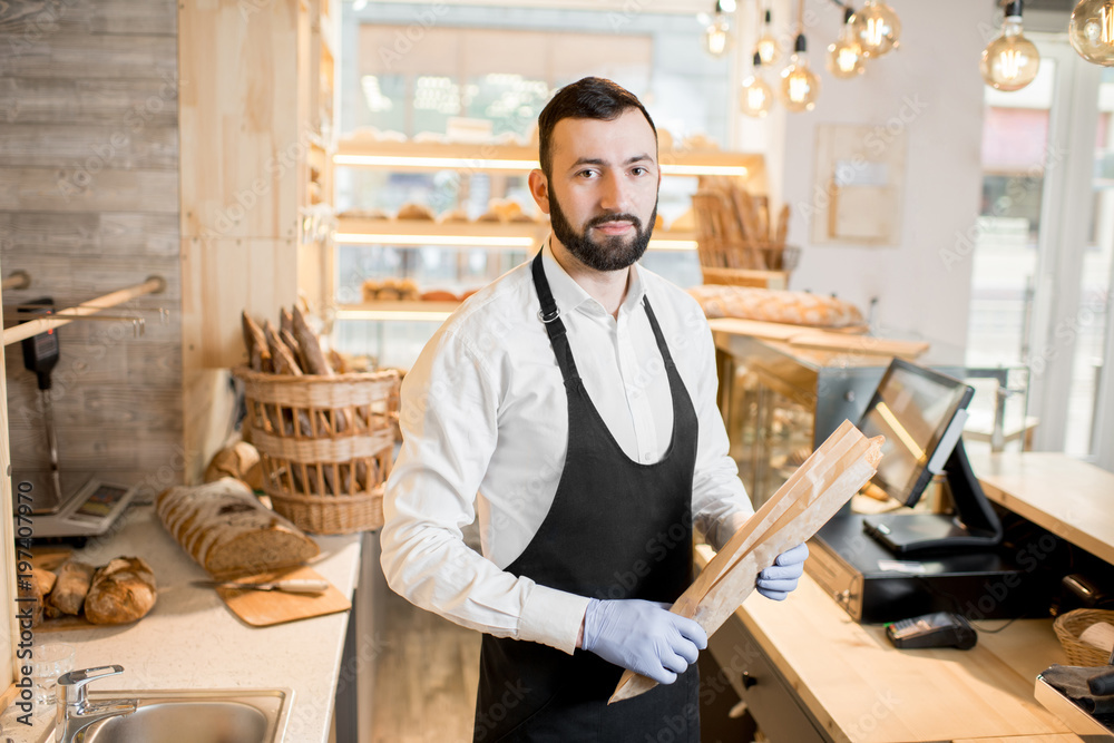 Portrait of a bread seller standing with baguette in the beautiful store with bakery products