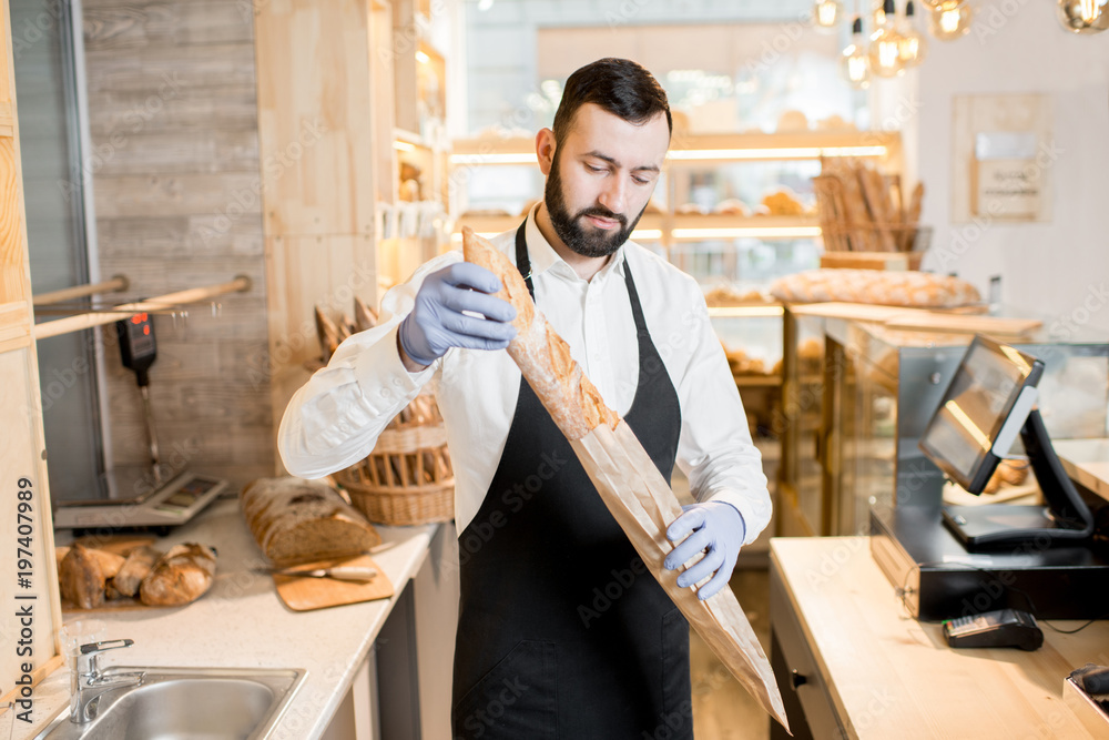 Portrait of a bread seller standing with baguette in the beautiful store with bakery products